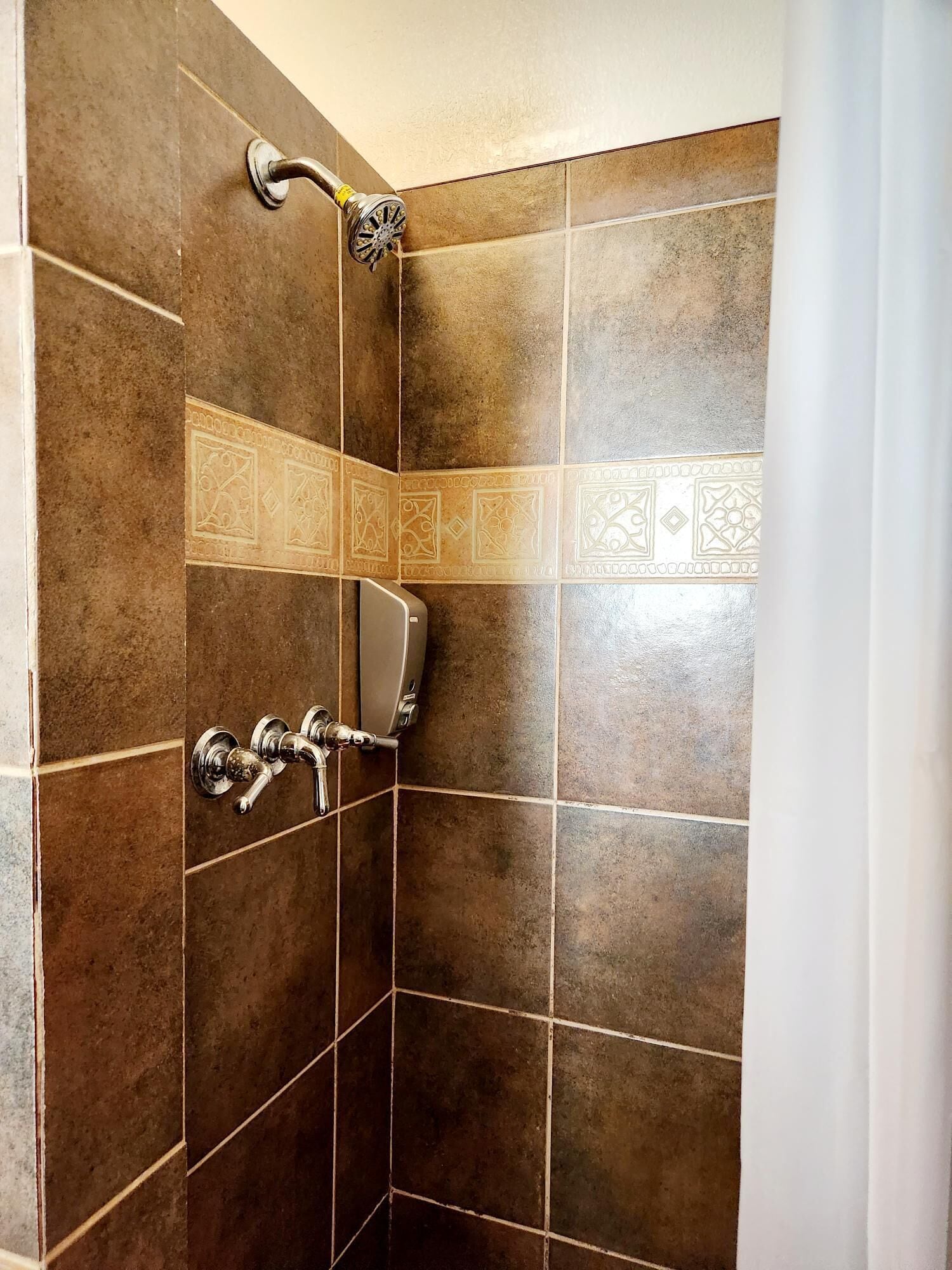 Zona de ducha con azulejos marrones y ducha de mano.
