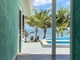 Vista desde una habitación a un área de piscina con palmeras y cielo despejado.