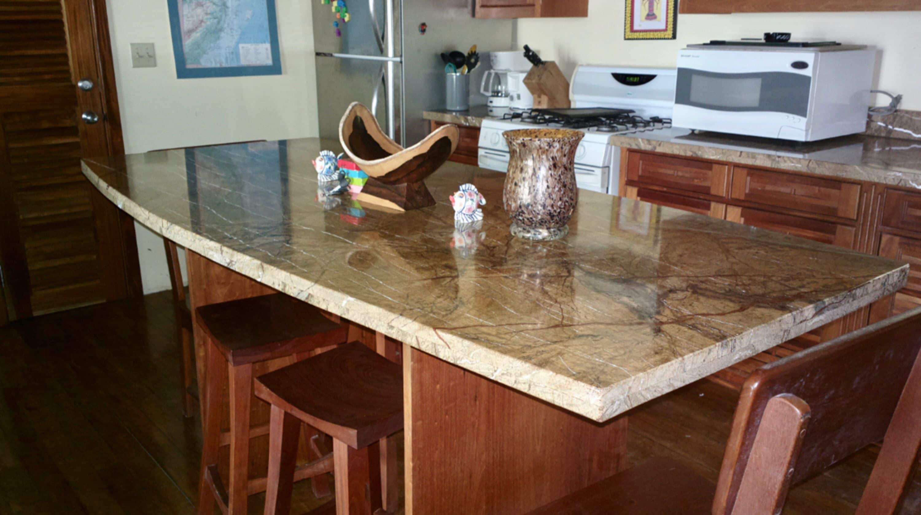 A kitchen with a marble countertop, wooden chairs, a stove, a microwave, and a refrigerator.