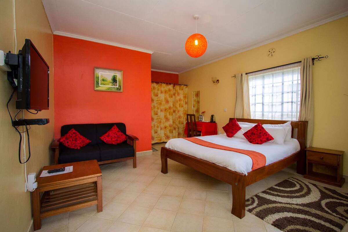 A hotel room with a bed, a sofa, a TV, and a window with curtains.