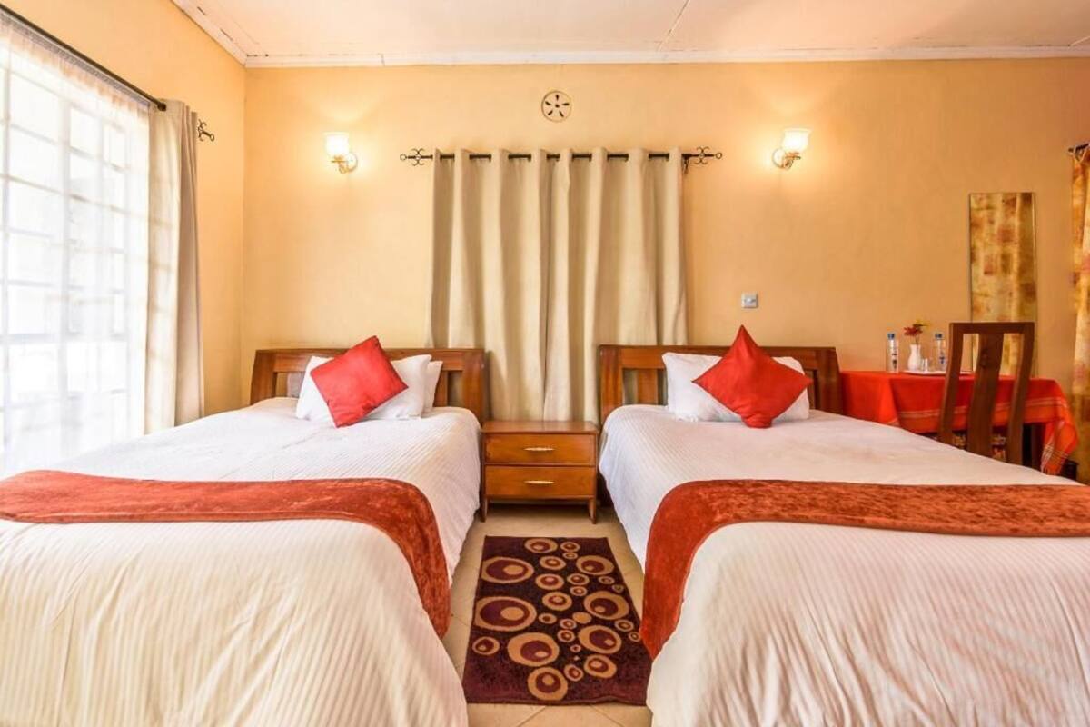 A hotel room with two beds, a small table, and a window with curtains.