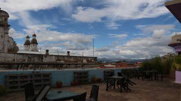 Una terraza en la azotea con mobiliario exterior, vista de un edificio histórico con cúpulas y cielo parcialmente nublado.