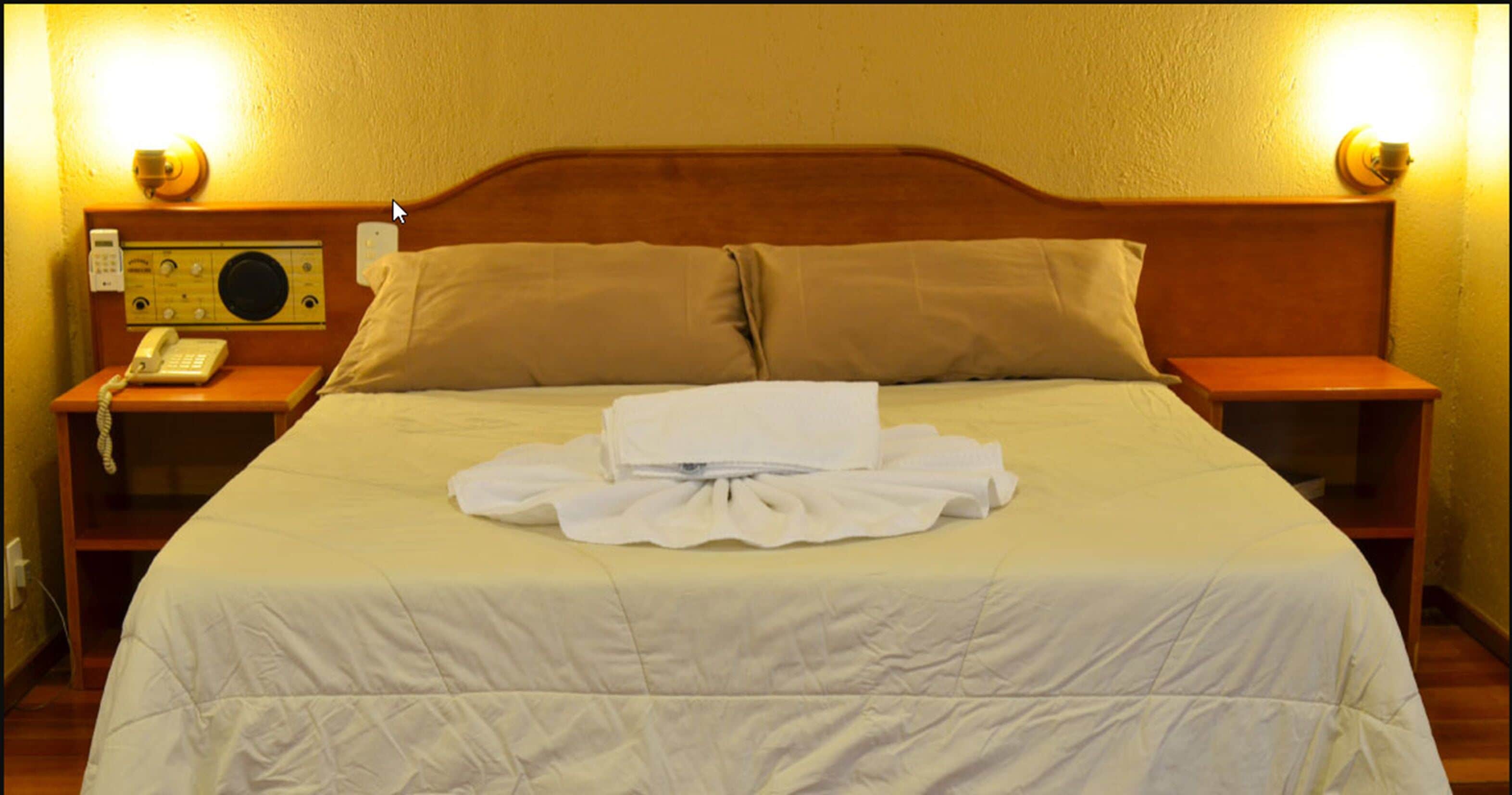A hotel room with a neatly made bed, a bedside telephone, and a radio on the nightstand.