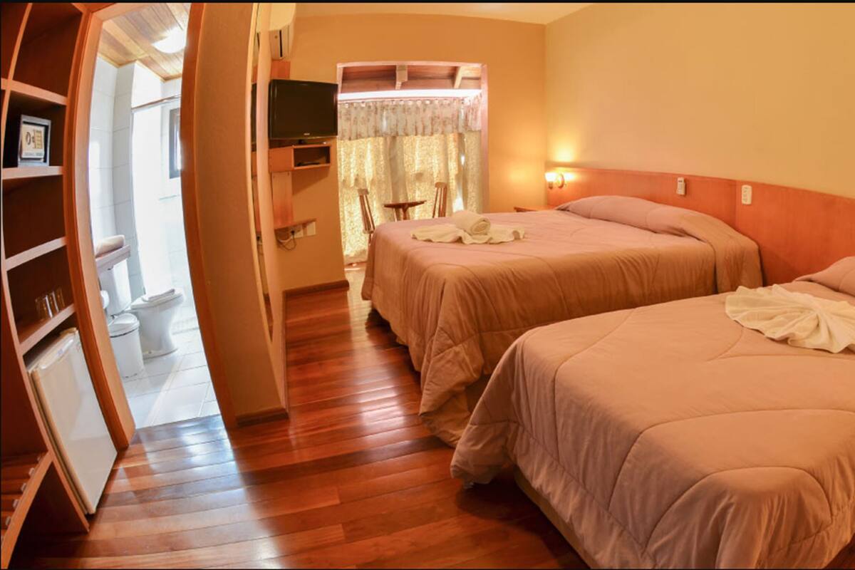 A hotel room with two beds, a small table, a television, and a bathroom visible through an open door.