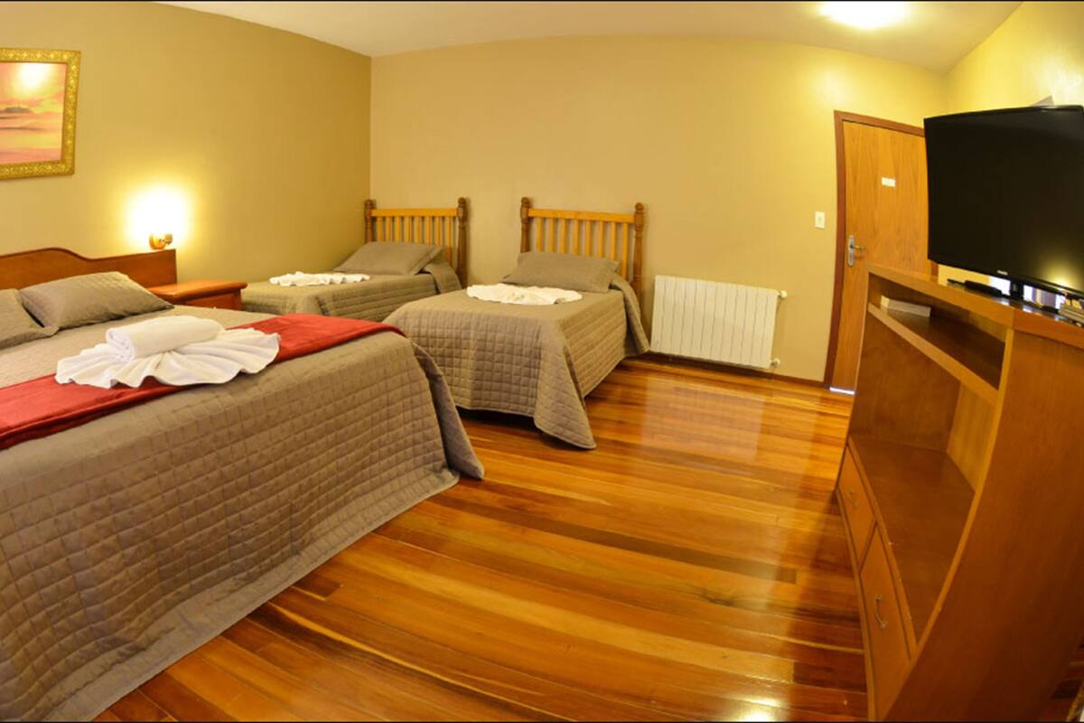 A hotel room with two single beds, a wooden floor, a television, and a painting on the wall.