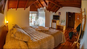 A bedroom with a large bed, a desk with a television, a chair, and a wooden coat rack. - Hotel Aconchego da Serra (Gramado)