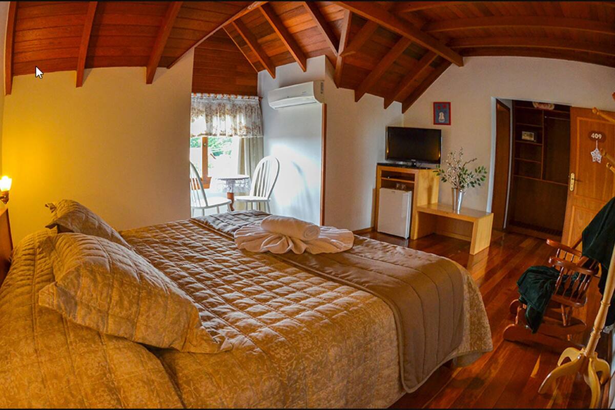 A bedroom with a large bed, a desk with a television, a chair, and a wooden coat rack.