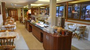 A buffet area with multiple tables and chairs, a central serving station, and large windows providing a view of the outside. - Hotel Aconchego da Serra (Gramado)