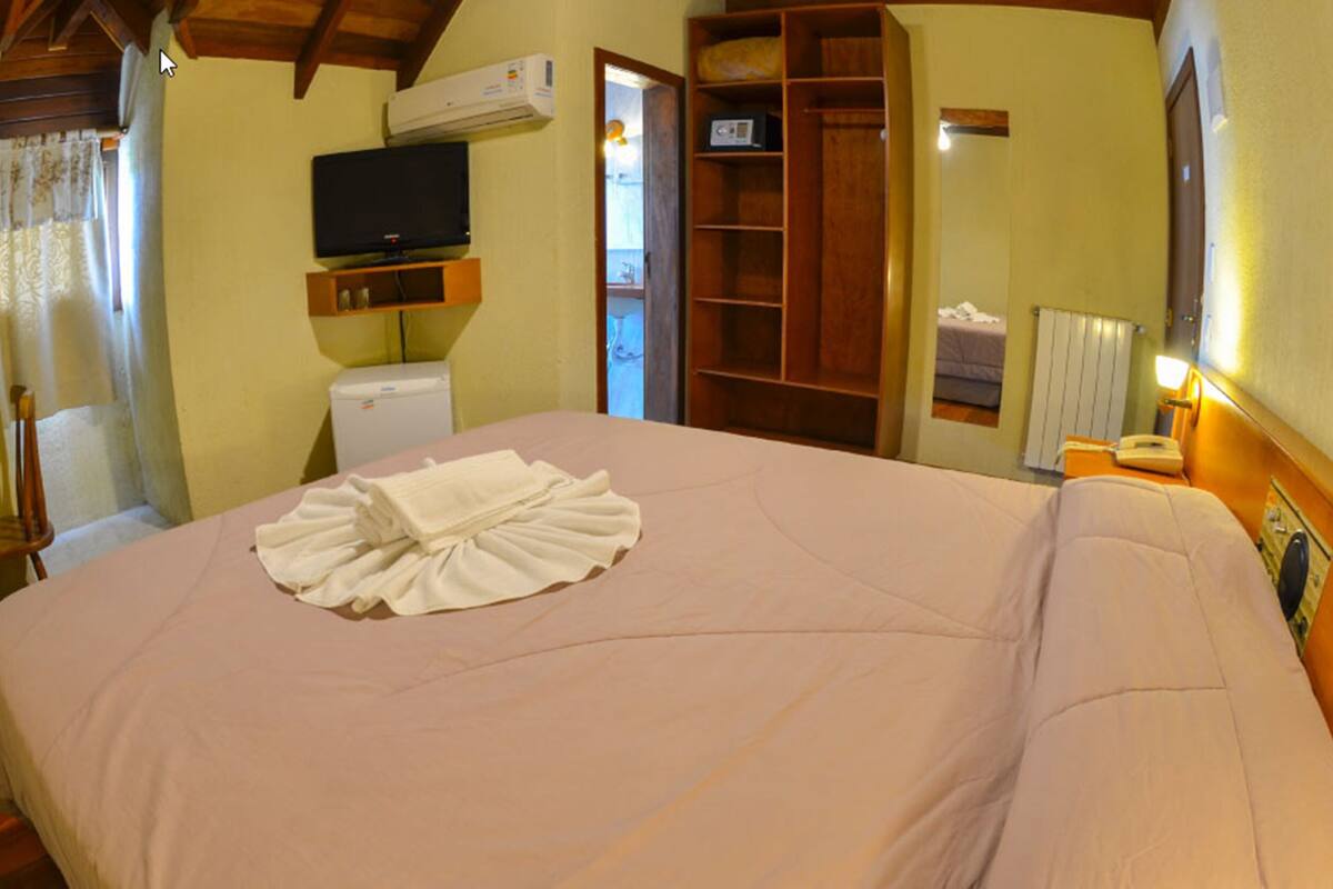 A hotel room with a large bed, a television, a wardrobe, and a small table with a lamp.