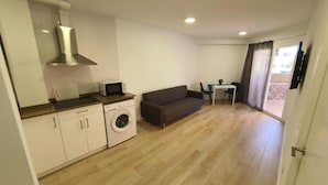 Un espacio habitable compacto con kitchenette, lavadora, sofá y comedor.
