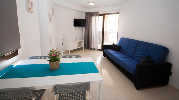 Una sala de estar con una mesa blanca, un sofá azul y un televisor montado en la pared.