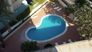Una piscina exterior con forma de corazón, rodeada por una solana con baldosas y equipada con sillones de descanso.