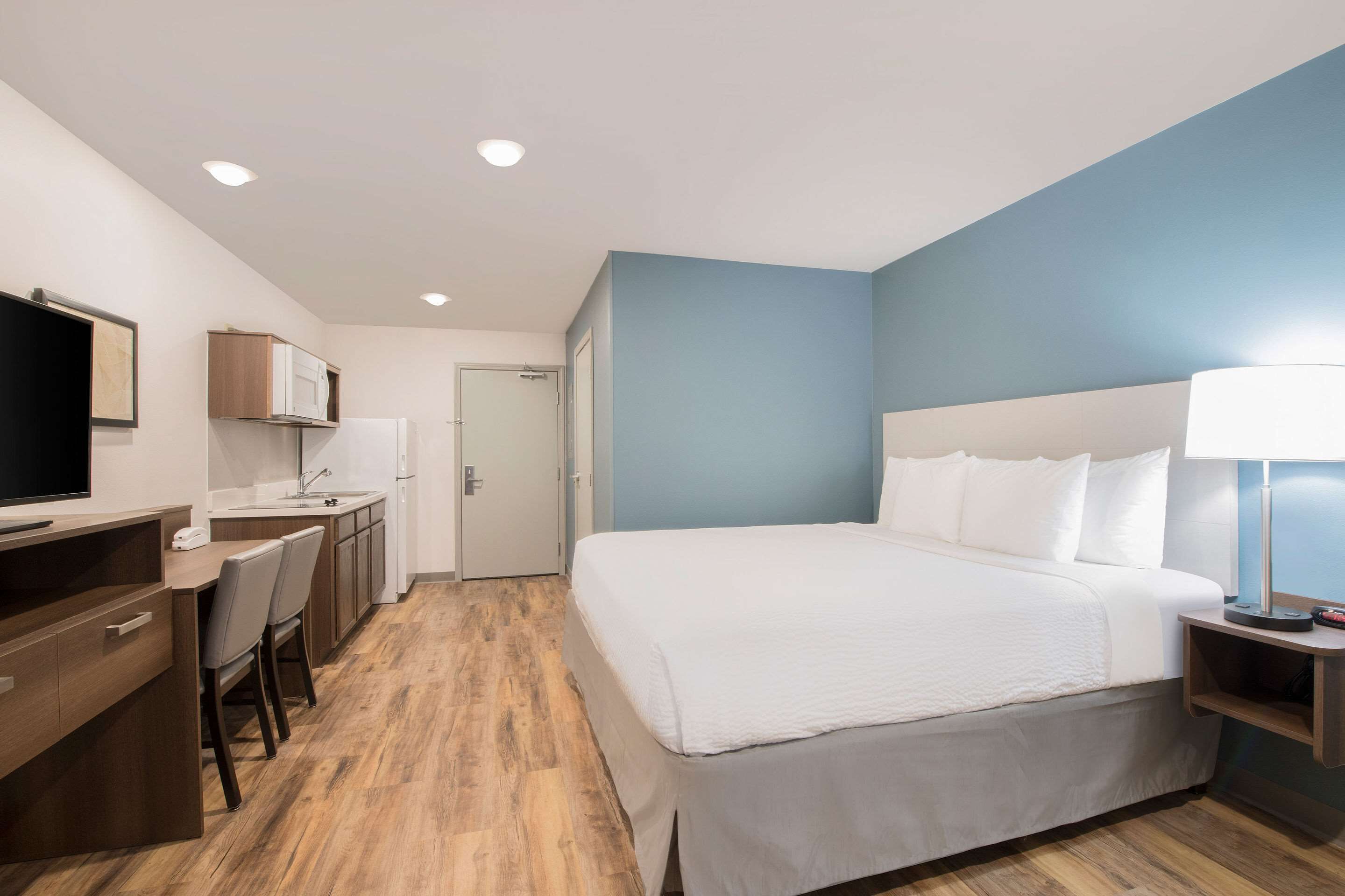A hotel room with a bed, a desk, a chair, a TV, a lamp, and a door.