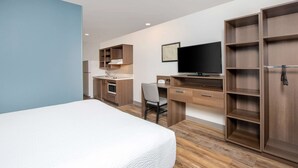 Et hotelværelse med seng, skrivebord med stol, fjernsyn og indbyggede hylder.