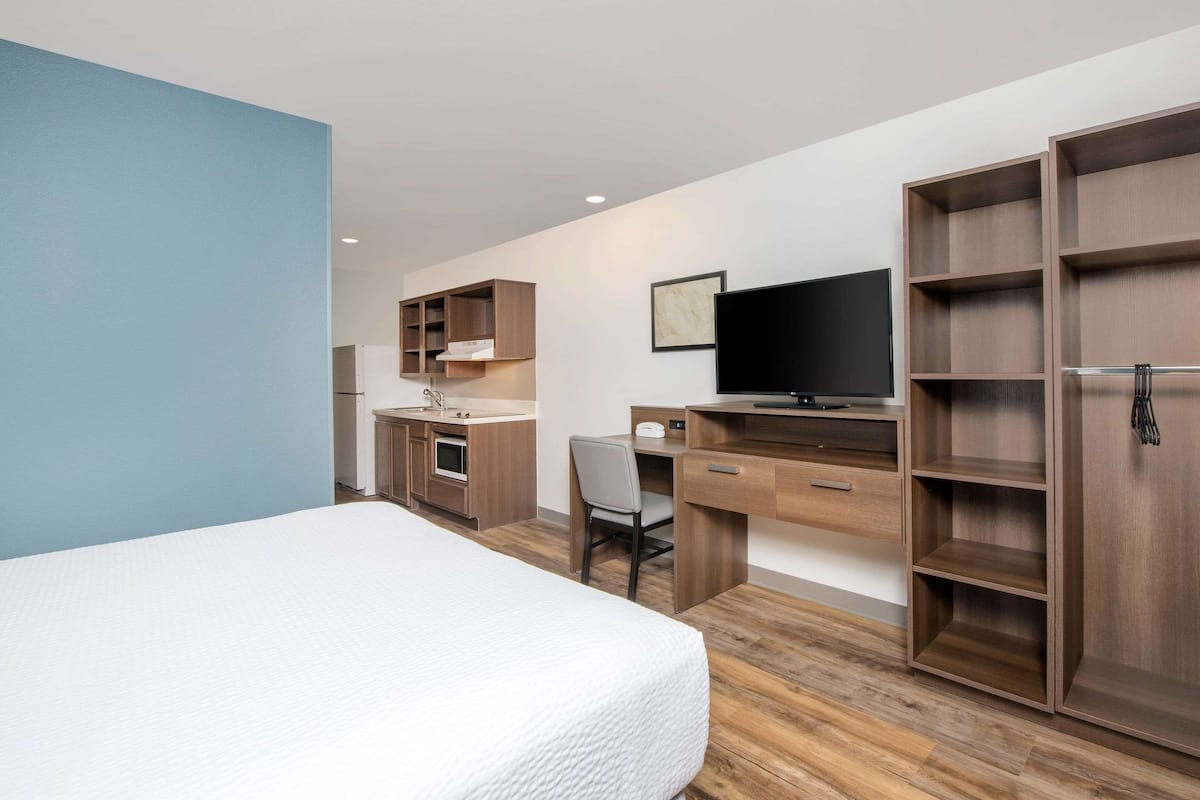 A hotel room with a bed, a desk with a chair, a TV, and built-in shelving.