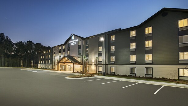 Et moderne hotel med flere etager, der har en markant indgangsparti med et overdækket område og et skilt med teksten "Woodspring Suites".