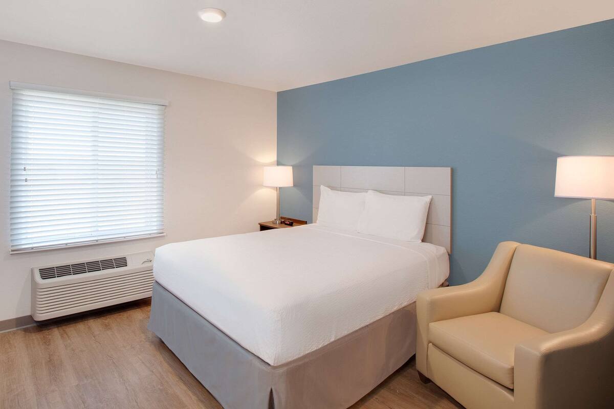Een hotelkamer met een groot bed, een stoel, een nachtkastje en een wandlamp.
