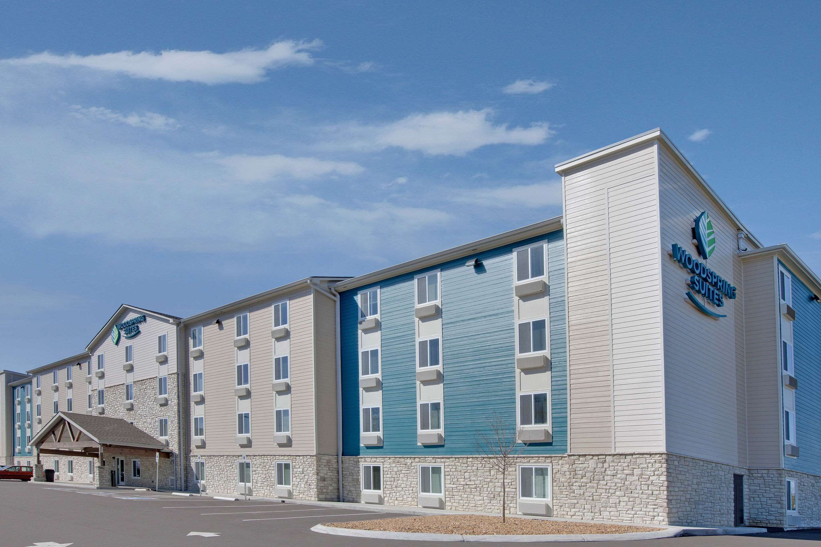 A multi-story hotel with a stone facade and blue accents, featuring a prominent logo on the side.