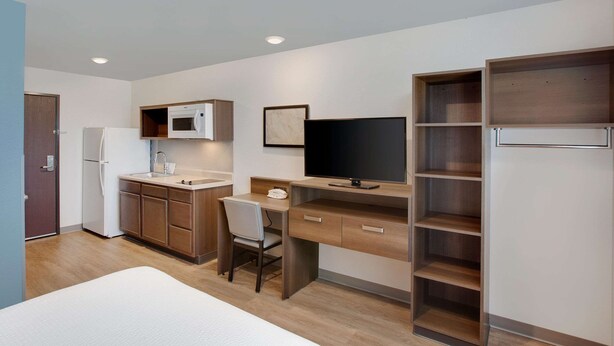 Een compacte kamer met een bed, een kitchenette, een bureau met stoel, een televisie en ingebouwde planken.