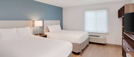A hotel room with two beds, a TV, a heater, and a window with blinds.