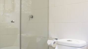A bathroom with a glass-enclosed shower, a white toilet, and a trash bin.