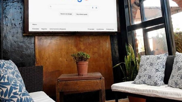 Een gezellig zitgedeelte met een groot raam, een bevestigd scherm waarop Google staat en een kleine tafel met een plant.