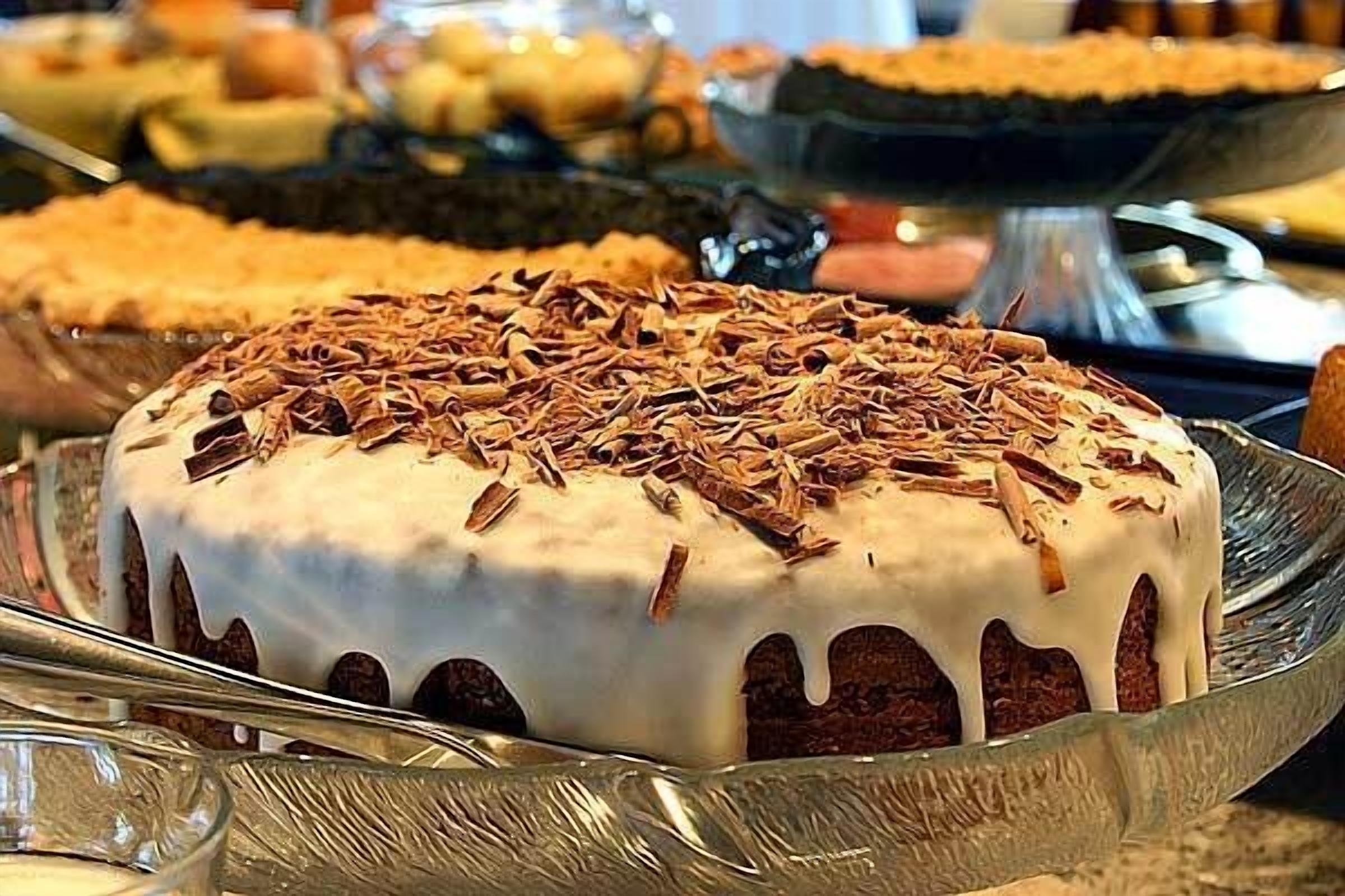 Pastís amb cobertura blanca i virutes de xocolata sobre un plat de vidre.