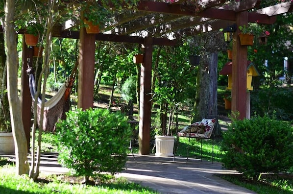 Una pérgola de madera con una hamaca, plantas en macetas y casas para pájaros en un exuberante jardín.