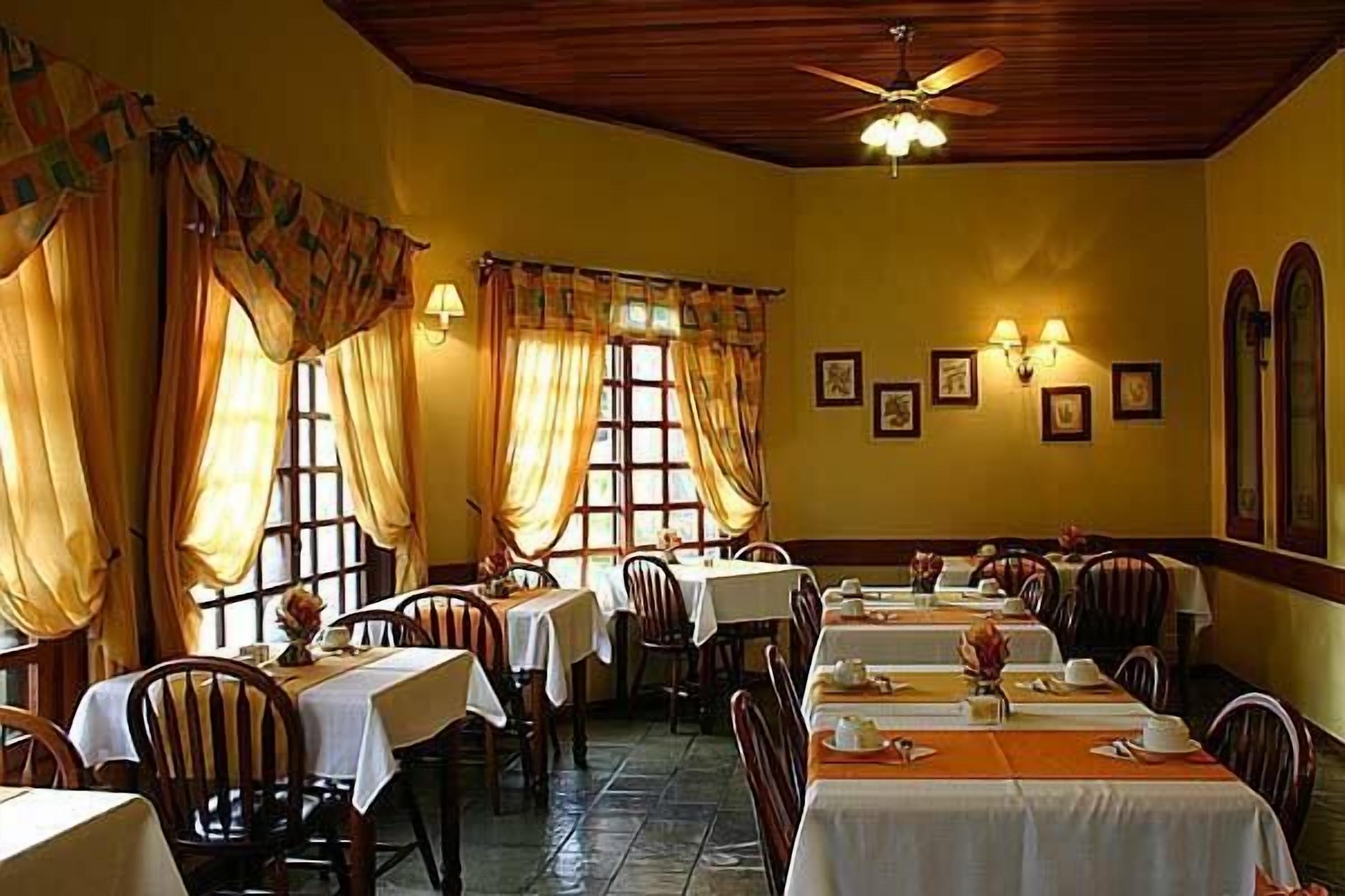 A dining area with tables set for service, wooden chairs, and a ceiling fan.