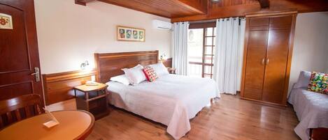 A cozy bedroom with a wooden ceiling, a bed with white bedding, a nightstand, a wooden chair, a small table, and a wardrobe.