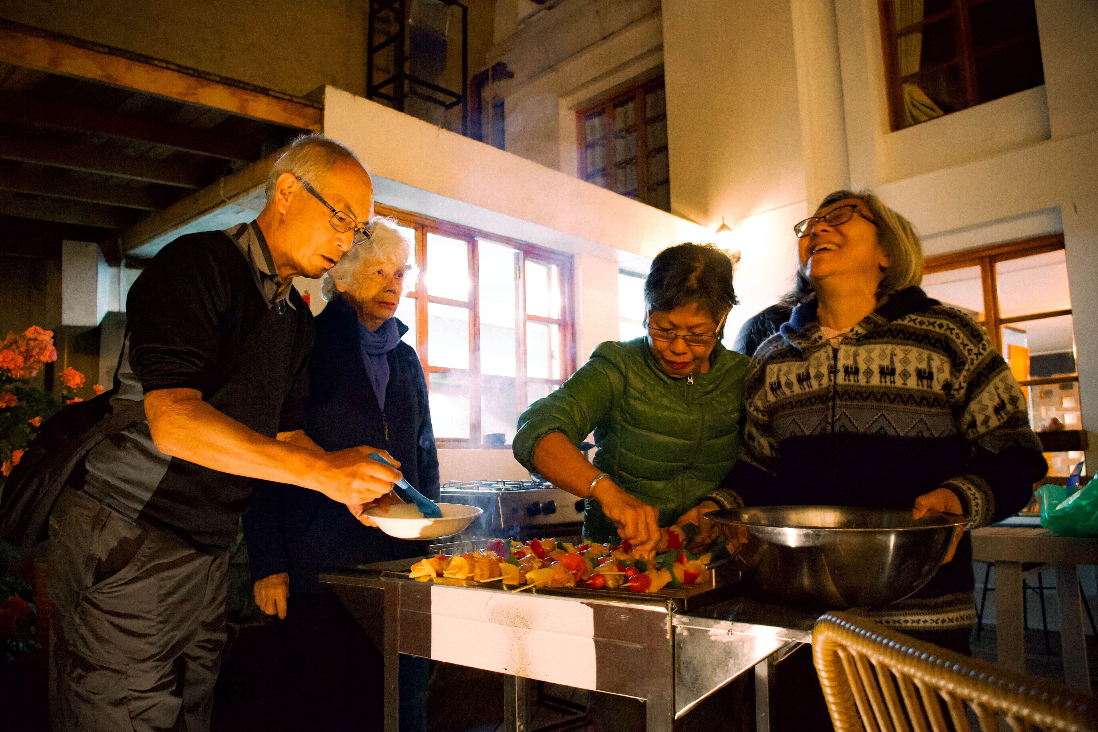 A group of people preparing food in a kitchen with a large metal bowl and skewers.