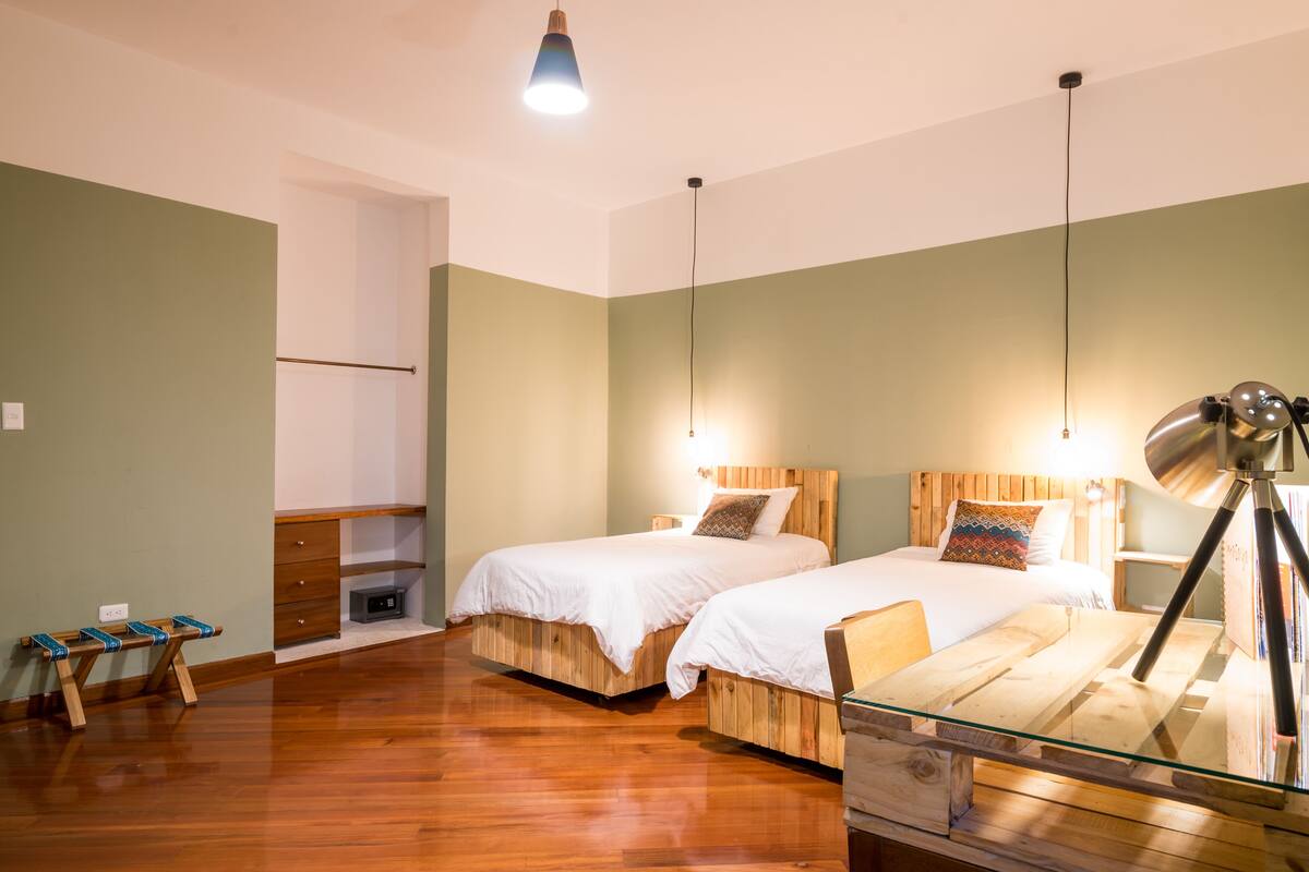 A room with two wooden beds, a glass table, and a hanging lamp.
