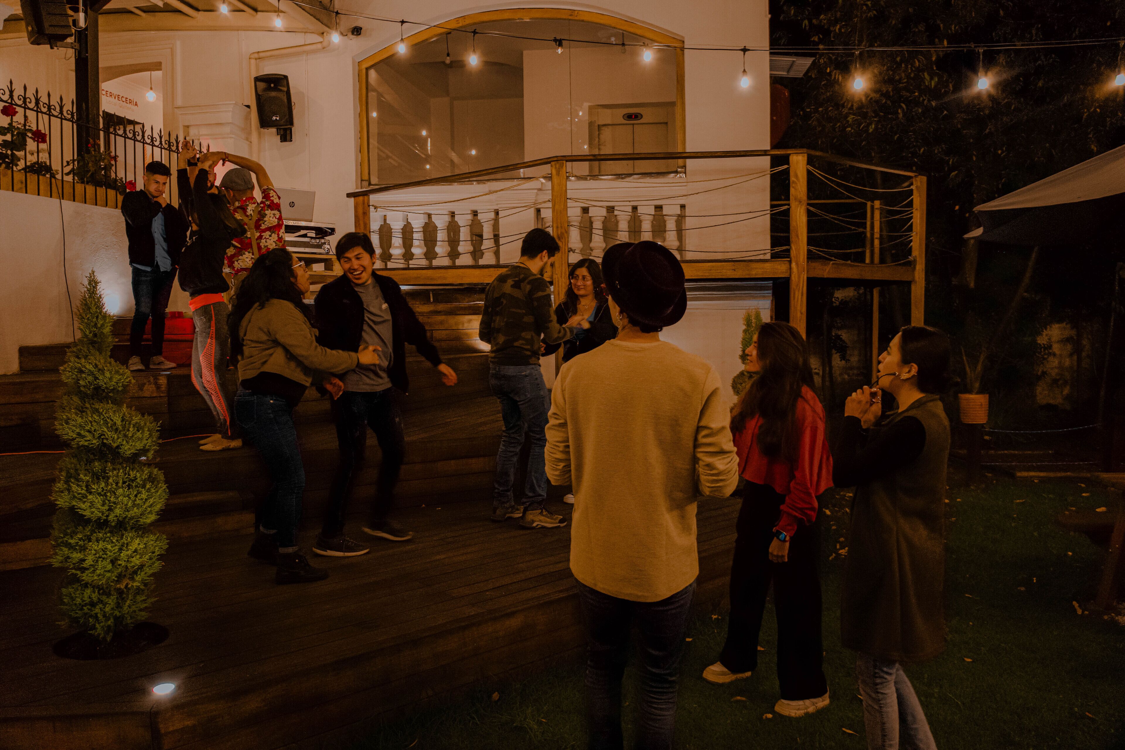 A group of people gathered around a wooden staircase in an outdoor setting, possibly a patio or terrace area.