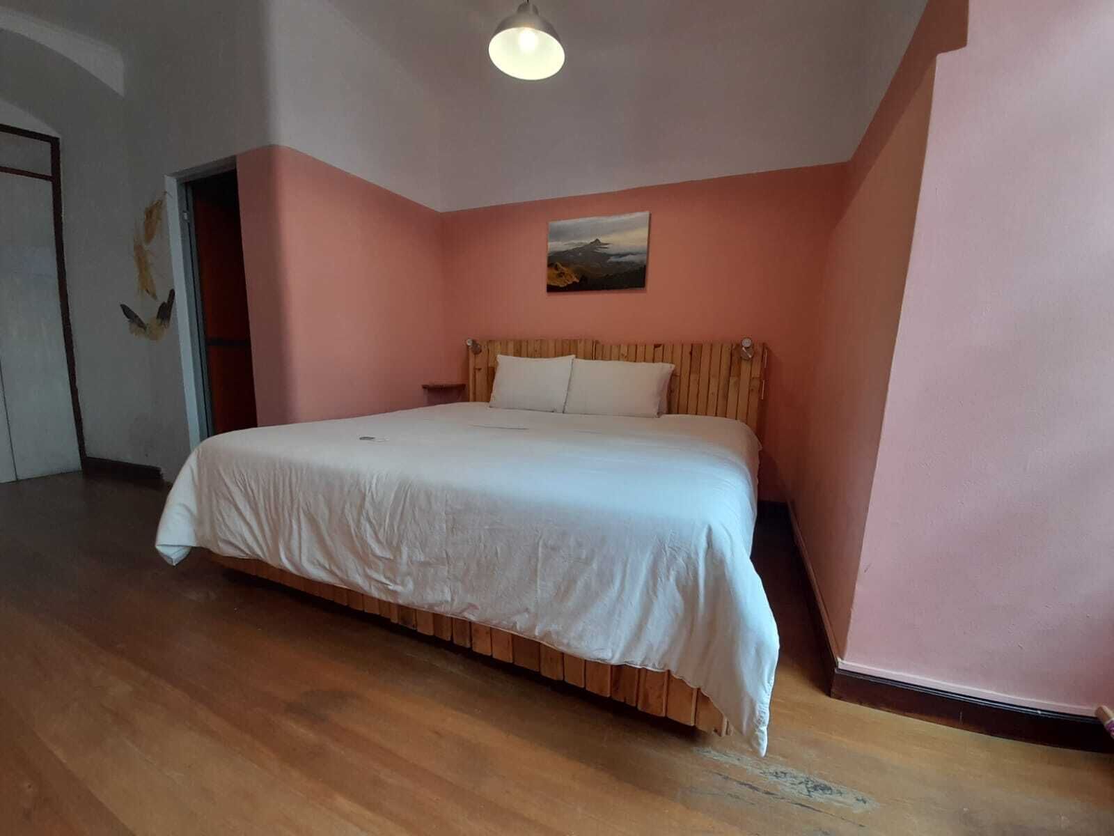 A bedroom with a wooden bed frame, white bedding, and a painting on the wall.