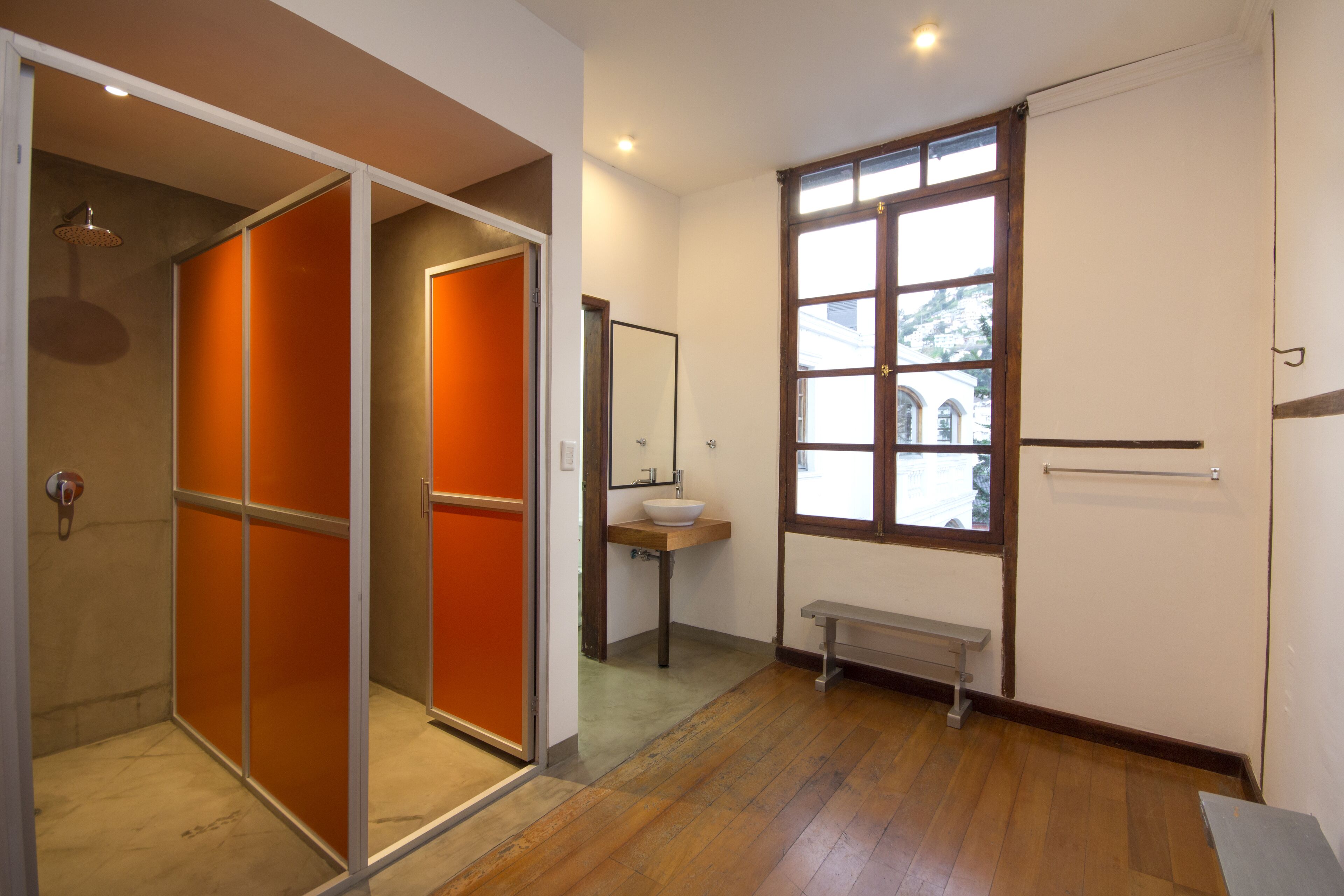 A bathroom with a wooden floor, a sink, a bench, and a window with a view of buildings outside.