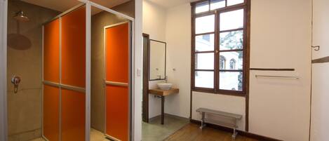 Une salle de bain avec un plancher en bois, un lavabo, un banc et une fenêtre donnant sur les bâtiments à l’extérieur.