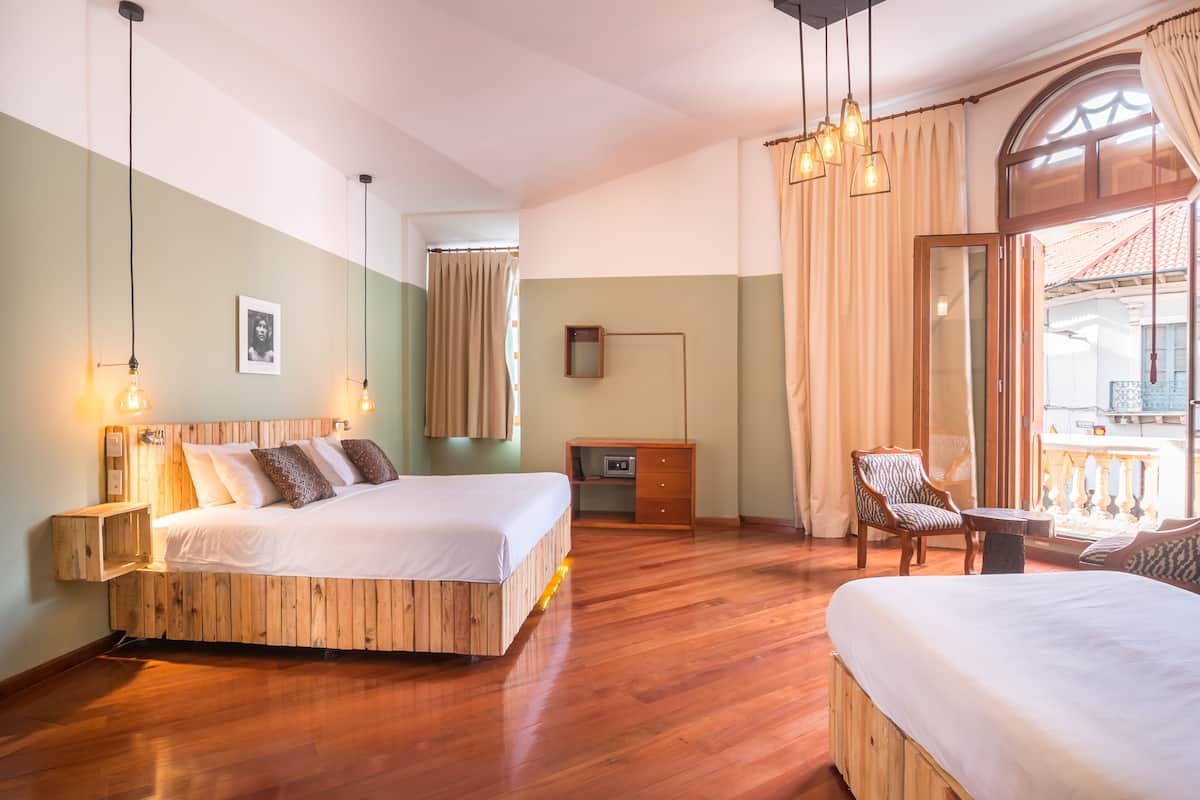 A hotel room with a wooden bed, a desk, a chair, and a balcony with a view.