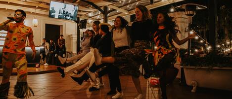 A group of people dancing in a well-lit indoor space with a tiled floor and a television mounted on the wall.