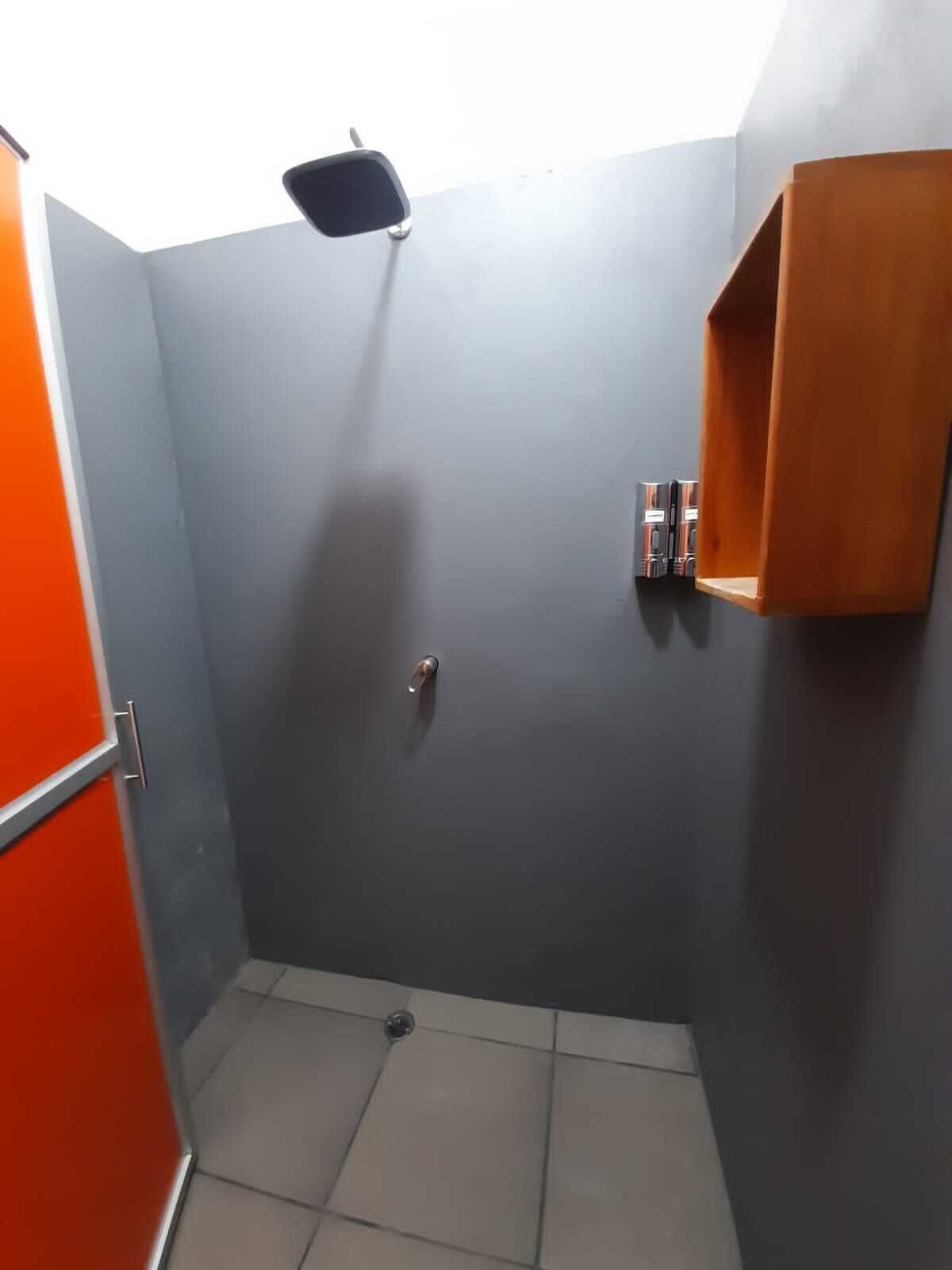 Un baño pequeño y cerrado, con una pared gris, un estante de madera y una puerta.