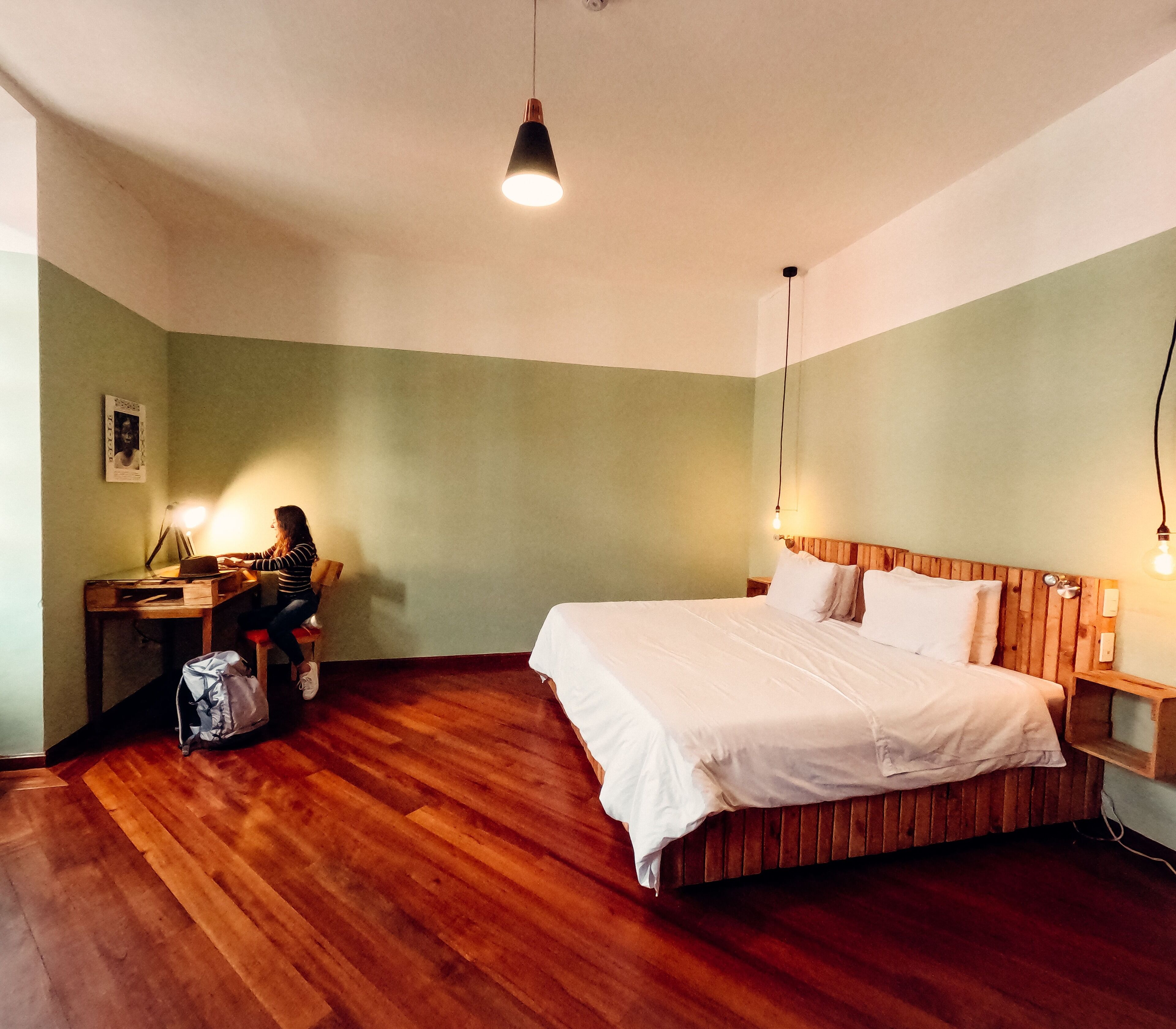 Een slaapkamer met een houten bed, een bureau met stoel, en een hanglamp.