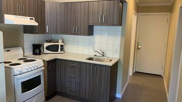 A compact kitchen with dark wood cabinets, white countertops, a built-in microwave, a stove, and a sink.