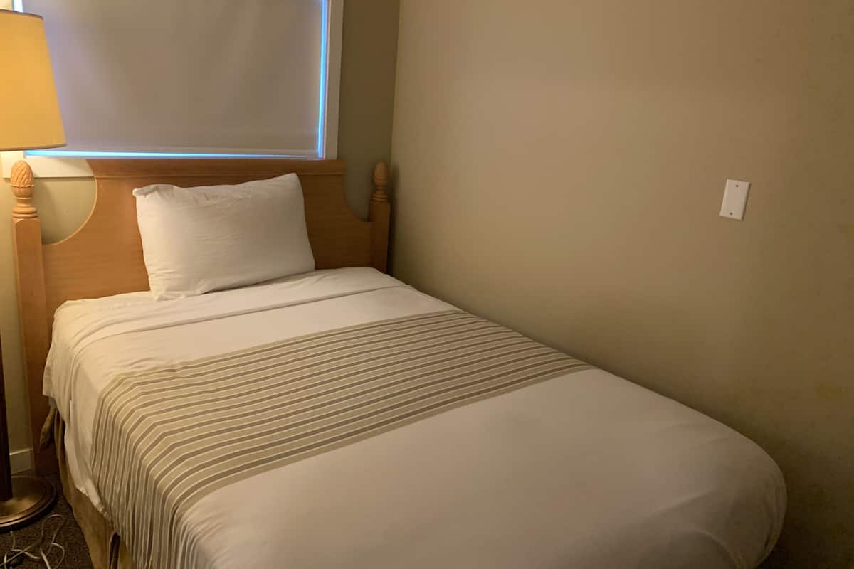 Un lit simple avec une tête de lit en bois, un oreiller blanc et une couvre-lit à rayures.