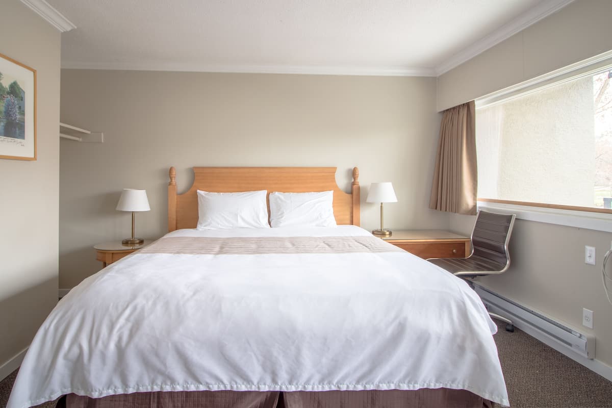 Une chambre d’hôtel avec un grand lit, deux tables de chevet avec des lampes, une chaise et une fenêtre avec des rideaux.