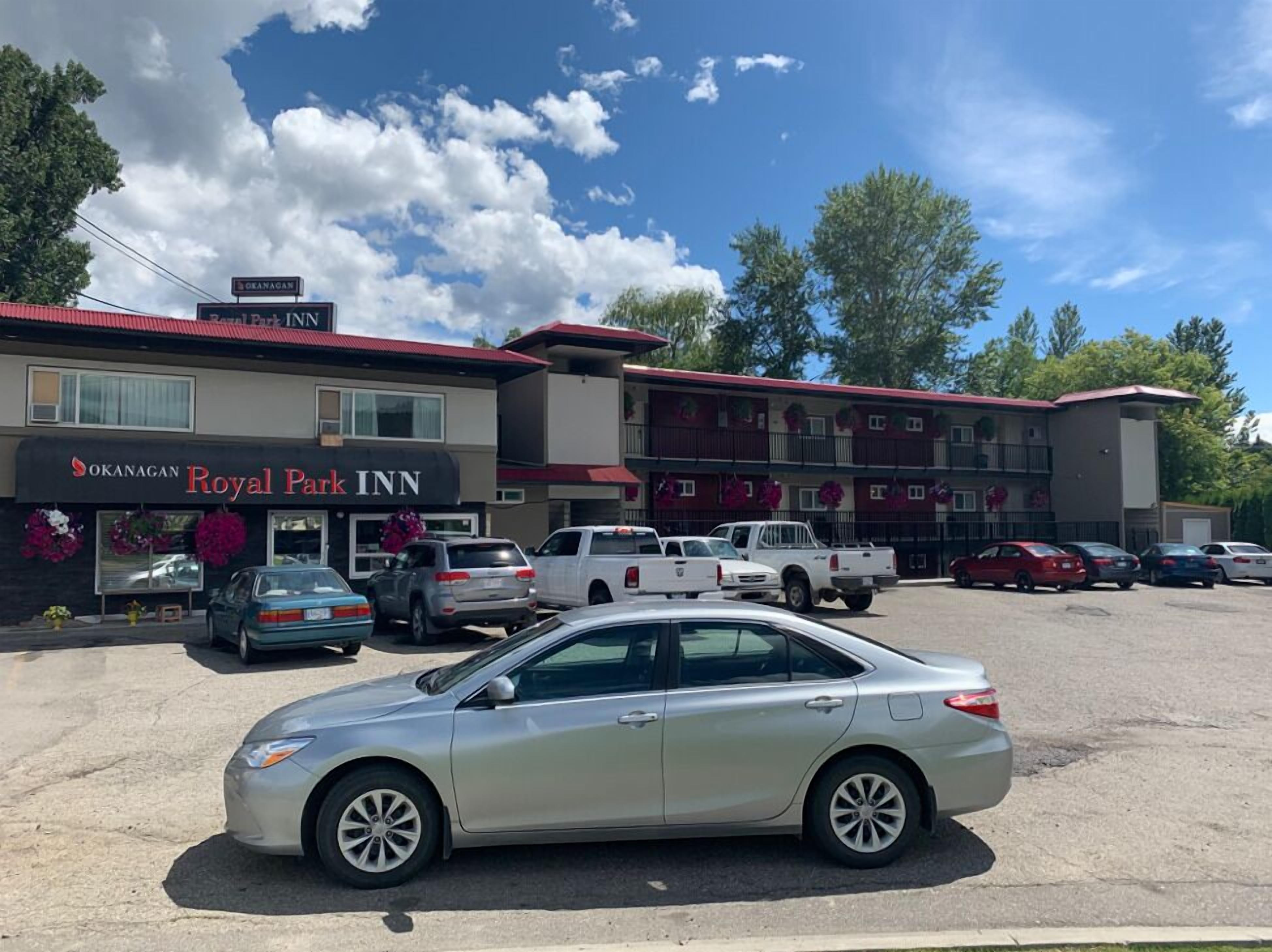 Ett hotell med en skylt som visar namnet ”Okanagan Royal Park Inn” och en parkeringsplats med flera bilar.