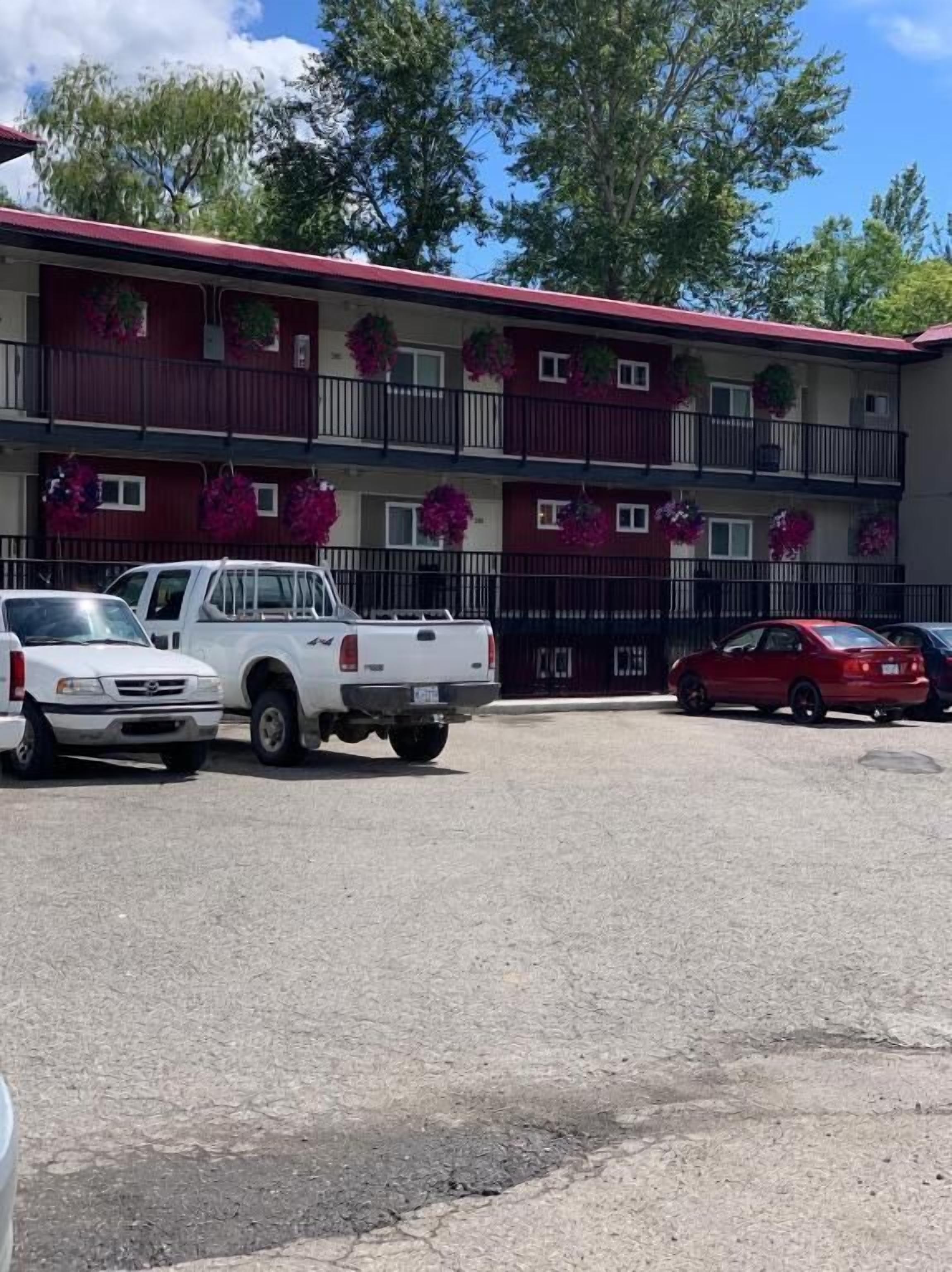 A multi-story building with balconies, a parking lot, and vehicles parked in front.