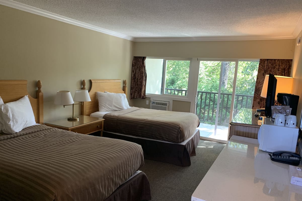Une chambre d’hôtel avec deux lits, un bureau avec un téléphone et un balcon donnant sur la verdure.