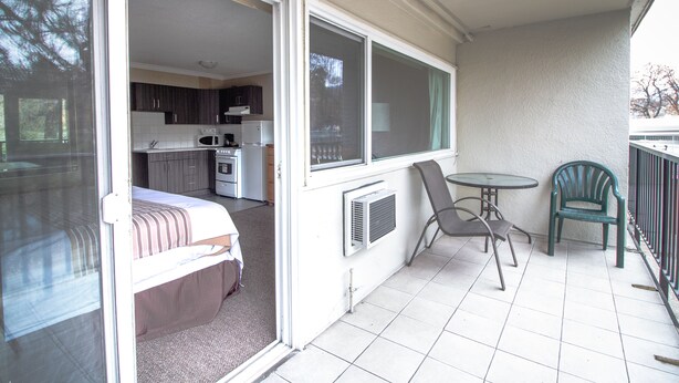 Een balkon met een bed, een tafel, twee stoelen en uitzicht op een keuken en woongedeelte.