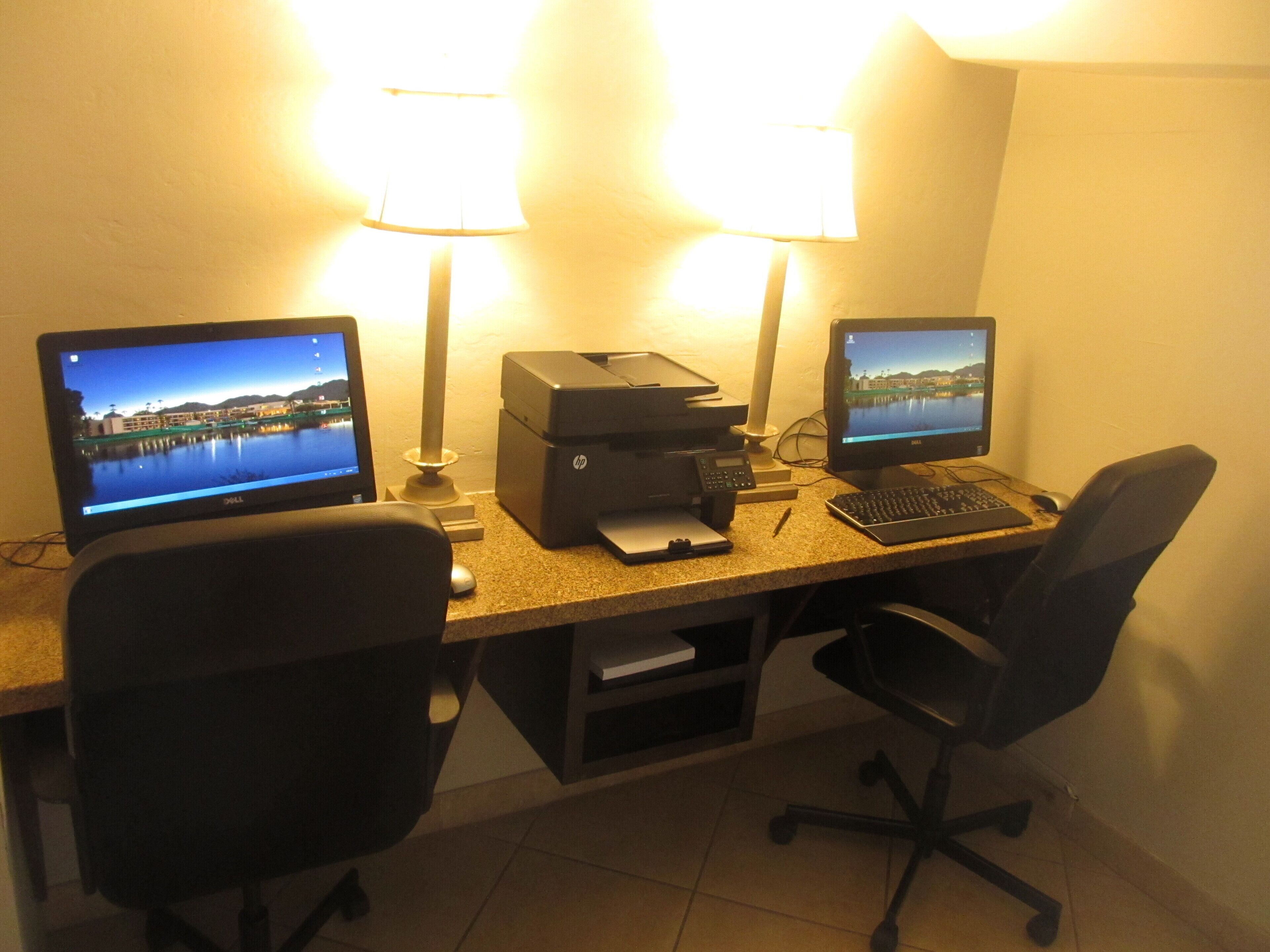 A desk with two monitors, a printer, and two office chairs.