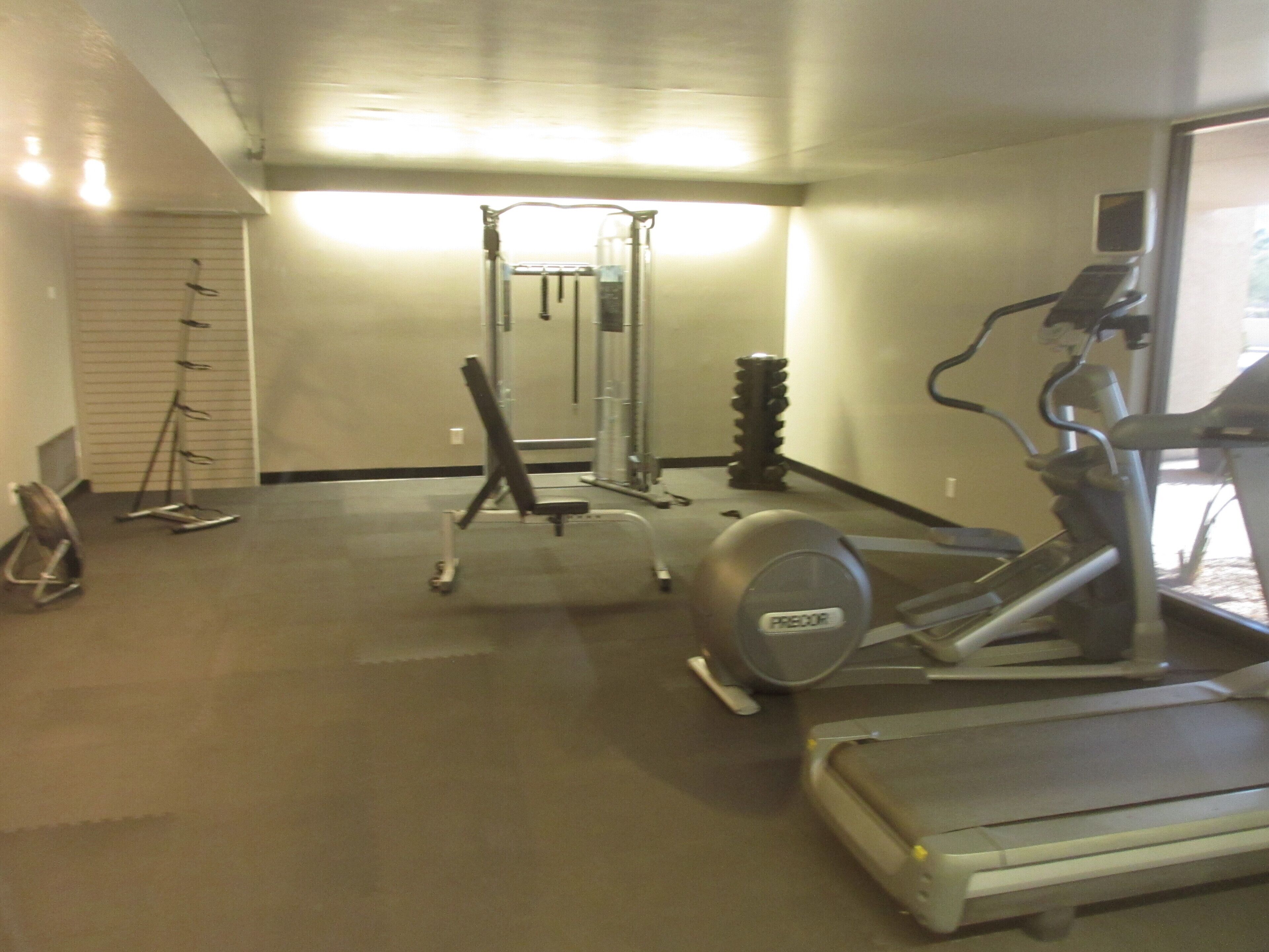 A gym with cardio machines, weightlifting equipment, and a mirror.