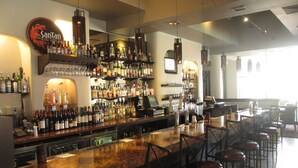 Een bar met verschillende drankflessen, glazen en een kassa.